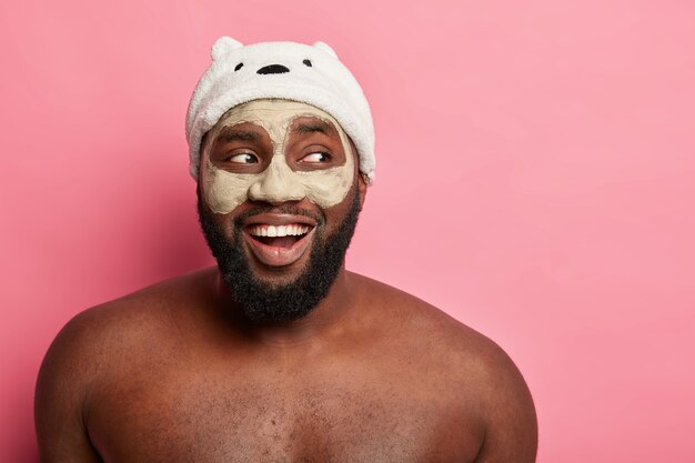 Afro American man with clay mask, expresses positive emotions isolated