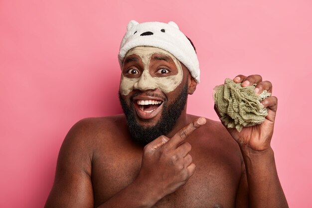 Afro American man with clay mask, expresses positive emotions isolated