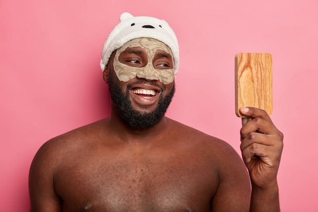 Afro American man with clay mask, expresses positive emotions isolated