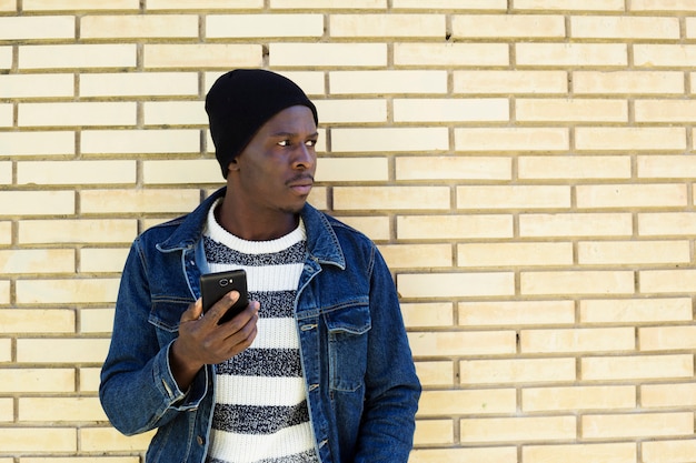 Afro american man with smartphone in front of wall