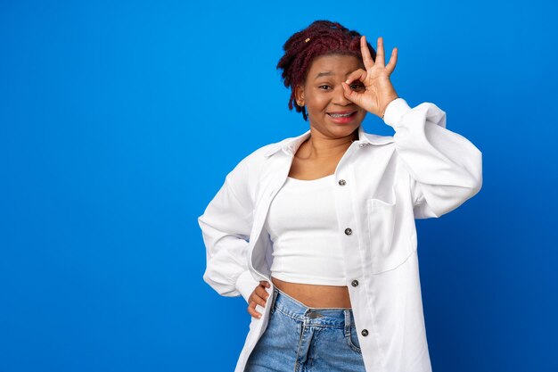 Afro american woman in white shirt showing ok sign on blue background