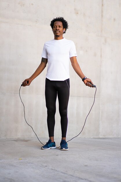 Afro athletic man doing exercise and jumping the rope outdoors