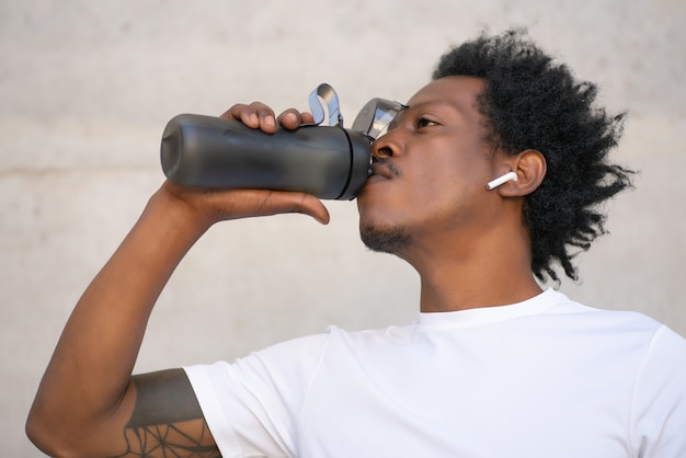 Free photo afro athletic man drinking water and relaxing after work out outdoors. sport and healthy lifestyle concept.