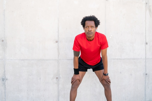 Foto gratuita uomo atletico afro che riposa dopo l'allenamento all'aperto. sport e concetto di stile di vita sano.