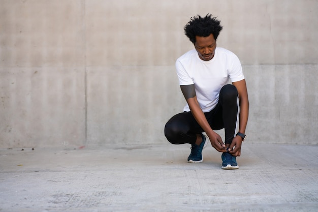 Afro athletic man tying his shoelaces and getting ready for work out outdoors. Sport and healthy lifestyle concept.