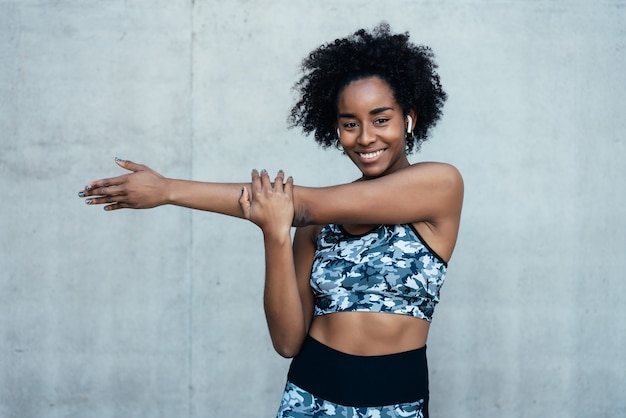 Afro athletic woman stretching her arms and warming up before exercise outdoors.