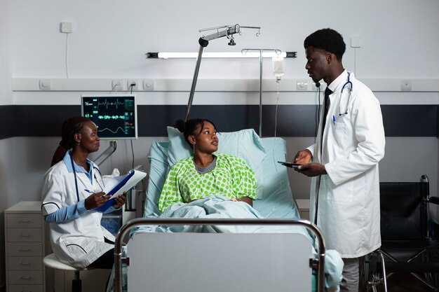 Afro doctors consulting young adult in hospital ward