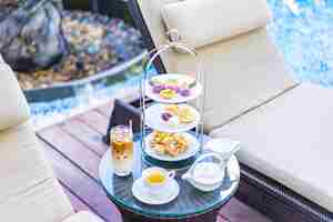無料写真 プールの周りの椅子の近くのテーブルでラテコーヒーと熱いお茶とアフタヌーンティーセット
