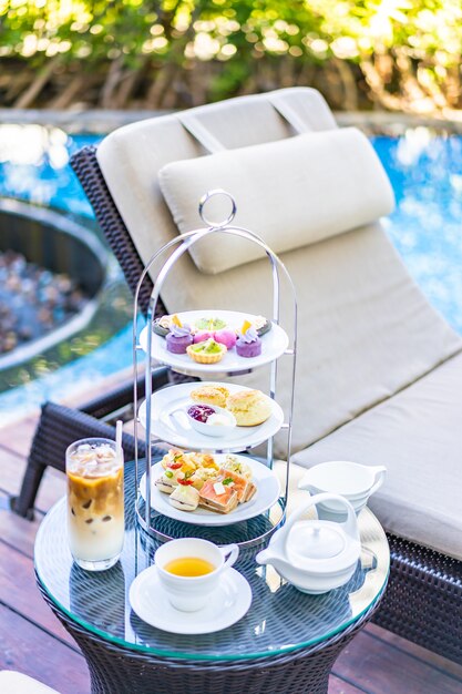 Afternoon tea set with latte coffee and hot tea on table near chair around swimming pool