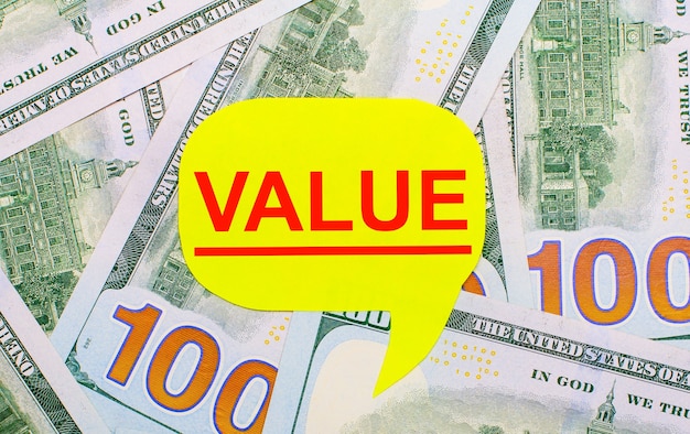 На фоне разбросанных по столу долларов - желтая фигурная карточка с текстом value. финансовая концепция