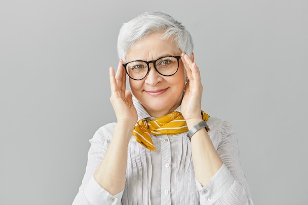 Бесплатное фото Возраст, оптика, очки и концепция зрения. улыбающаяся красивая элегантная зрелая женщина на пенсии с радостным выражением лица, поправляющая стильные очки в черной оправе, в рубашке и шарфе