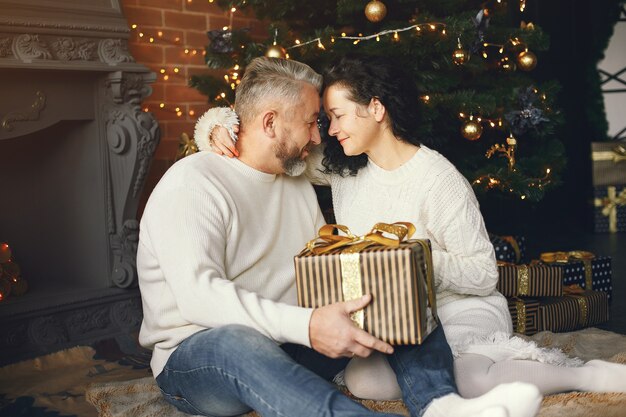 Age and people concept . Senior couple with gift box over lights background. Woman in a white knited sweatre.