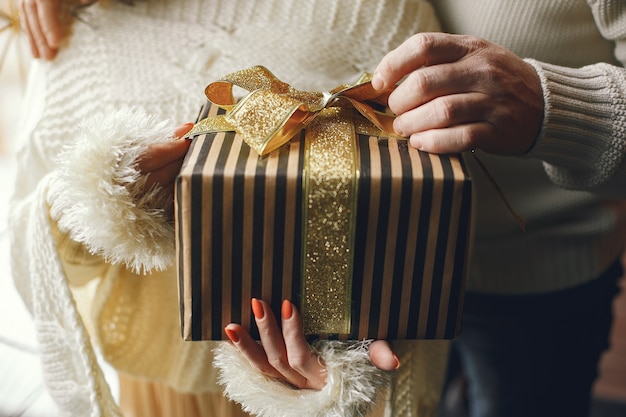 Concetto di età e persone. coppia senior con confezione regalo su sfondo di luci. donna in una felpa lavorata a maglia bianca.