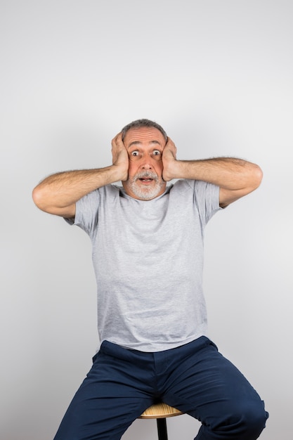 Free photo aged amazed man with hands on head on chair