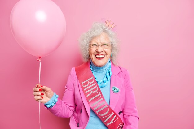 Aged curly haired senior wrinkled woman with inflated balloon celebrates birthday