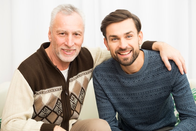 Aged happy man hugging young smiling guy on sofa