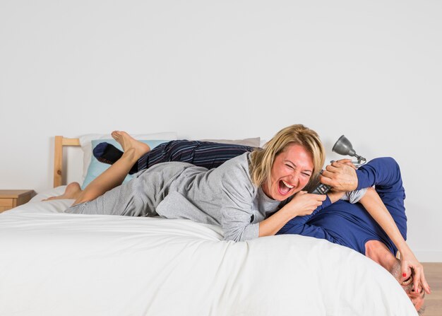 Free photo aged laughing woman wanting to take tv remote from man hands on bed