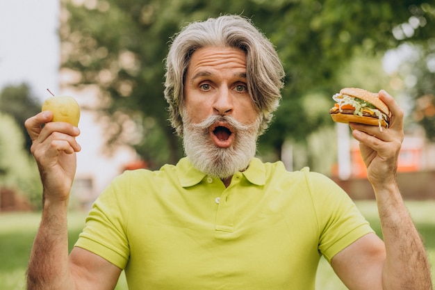 Aged man choosing between burger and apple