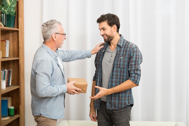 Aged man giving present to young happy guy