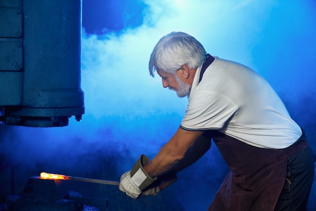 Free photo aged man holding heated steel under press machine