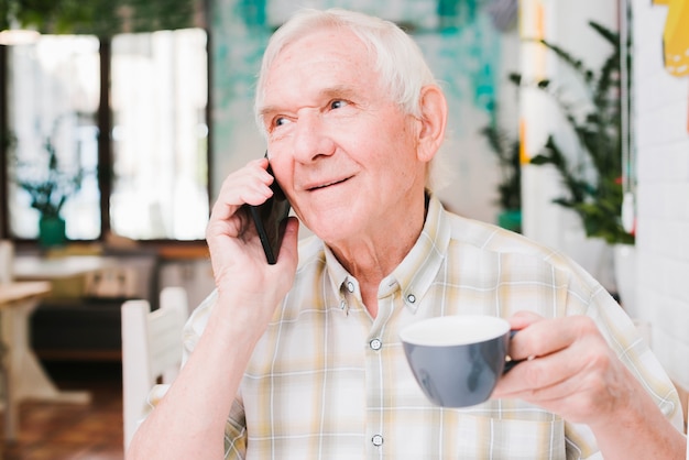 Aged man talking on phone with cup in hand