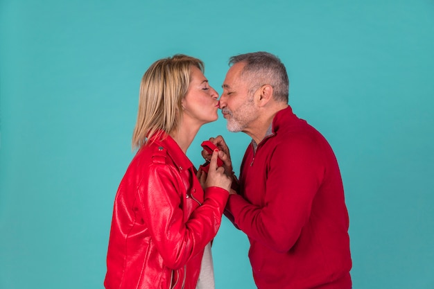 Aged man with jewellery box kissing with woman