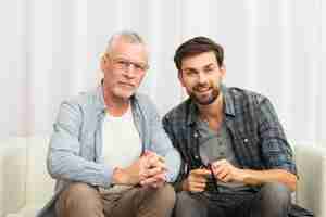 Free photo aged man and young happy guy clasping hands on sofa