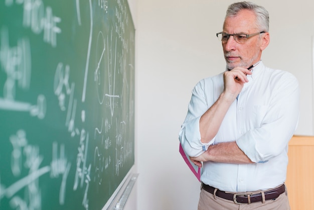 Aged math teacher thinking next to chalkboard