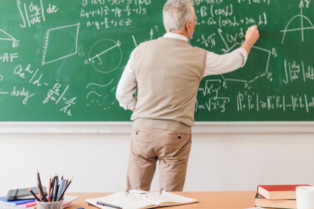 Aged math teacher writing equation on chalkboard