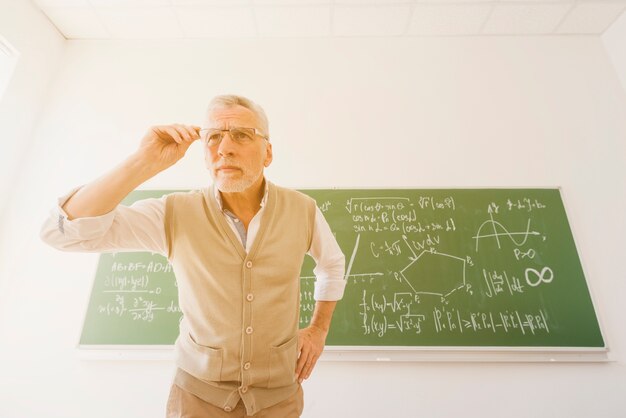 Aged professor looking through glasses in classroom