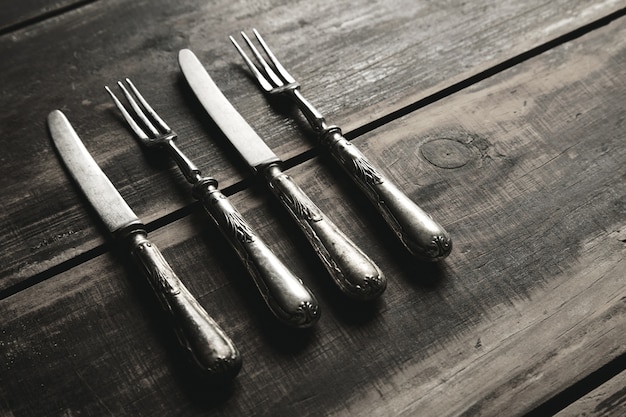 Aged retro vintage set of stainless steel forks and knives covered with patina isolated on brushed black wooden table side view