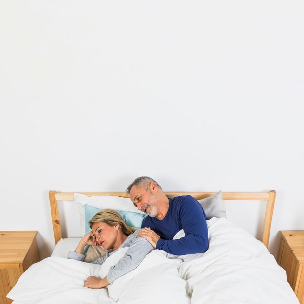 Aged sad woman lying near man on bed