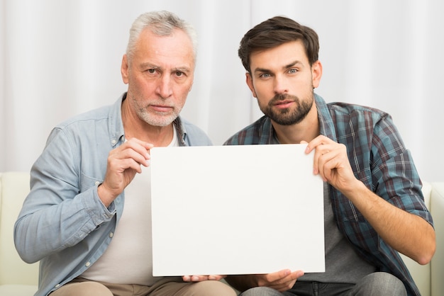 Пожилой серьезный мужчина и молодой парень, держа бумагу на диване