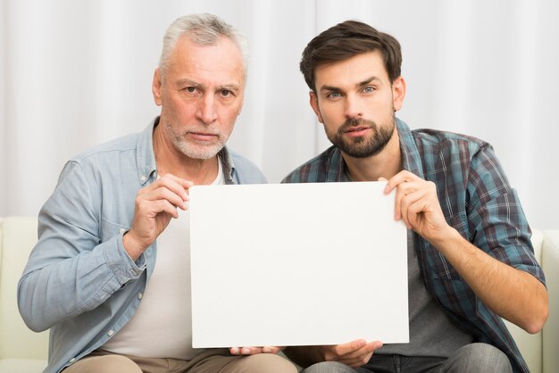 Aged serious man and young guy holding paper on sofa