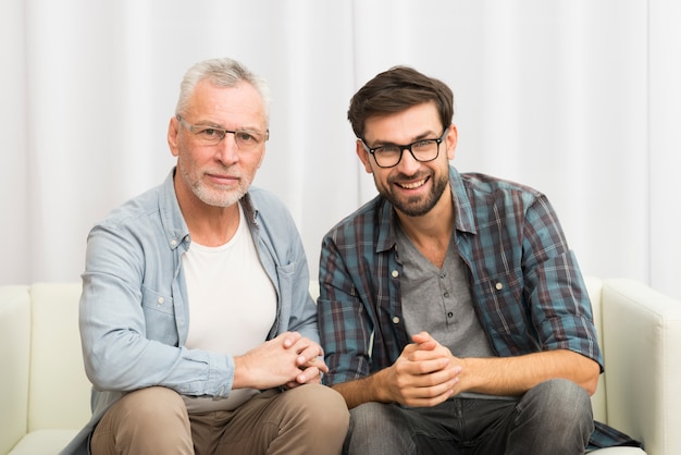 Aged smiling man and young happy guy clasping hands on sofa