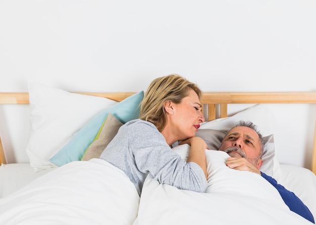 Пожилая женщина лежала возле грустного человека в пуховом одеяле на кровати