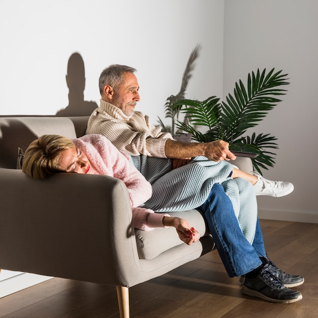 Aged woman and man with TV remote watching TV on sofa