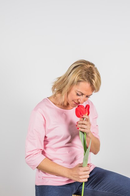 Aged woman in rose blouse smelling flower