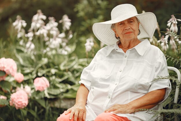 Aged woman sitting in the park. Grandma in a white hat.