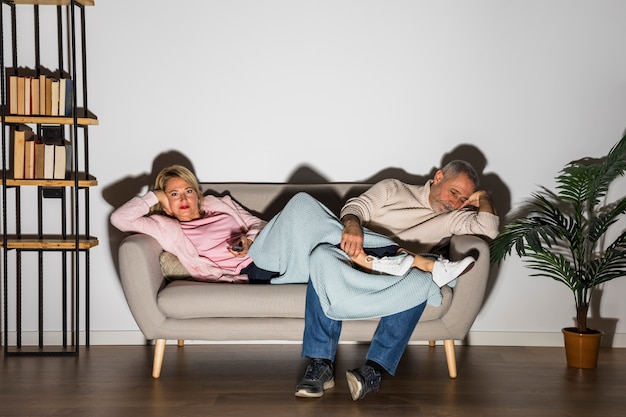 Free photo aged woman with tv remote and man watching tv on sofa