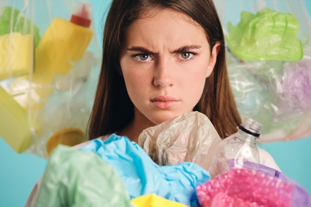 Aggressive girl with plastic waste around angrily looking in camera over colorful background isolated