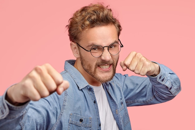 Free photo aggressive man bites with fists, has angry expression, defenses himself, clenches teeth from anger