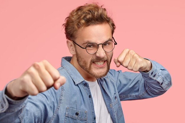 Агрессивный мужчина кусает кулаками, имеет гневное выражение лица, защищает себя, стиснет зубы от гнева