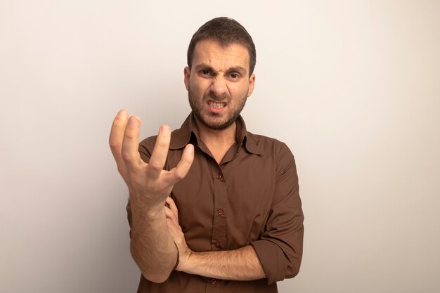 Aggressive young caucasian man putting hand on arm stretching out hand towards camera looking at camera isolated on white background with copy space