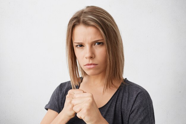 Aggressive young female keeping her fists ready to fight and defense herself against injustice or violence. Strong woman clenching fists as if boxing, looking with serious expression