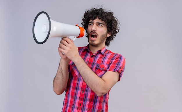 An aggressive young handsome man with curly hair in checked shirt holding megaphone and wanting to say something 