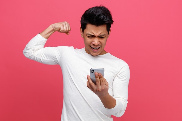 Агрессивный молодой человек, держащий и смотрящий на мобильный телефон, делает сильный жест