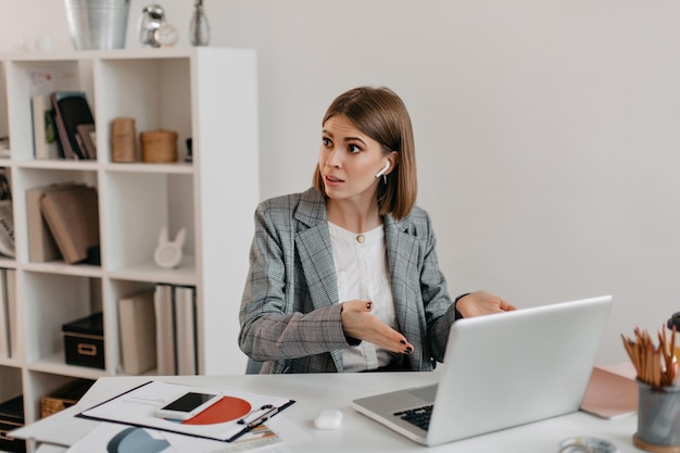 Agitated business woman in gray jacket speaks indignantly with employee standing outside camera