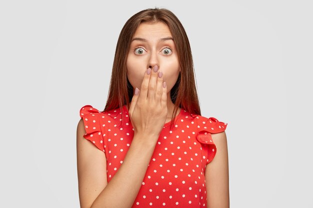 Agitated shocked woman with red lipstick posing against the white wall