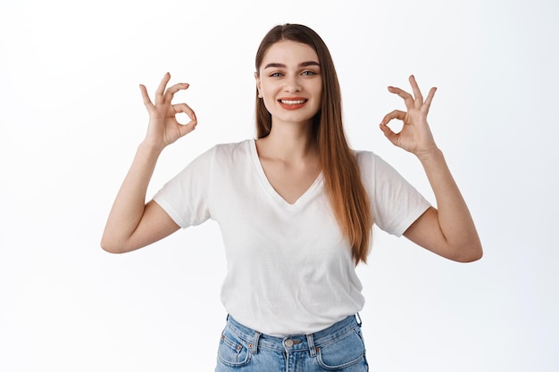 Free photo agree, recommend. smiling woman shows okay signs, ok gesture and nod, say yes, give approval, satisfied with good thing, praise choice, excellent job, good work, standing over white background